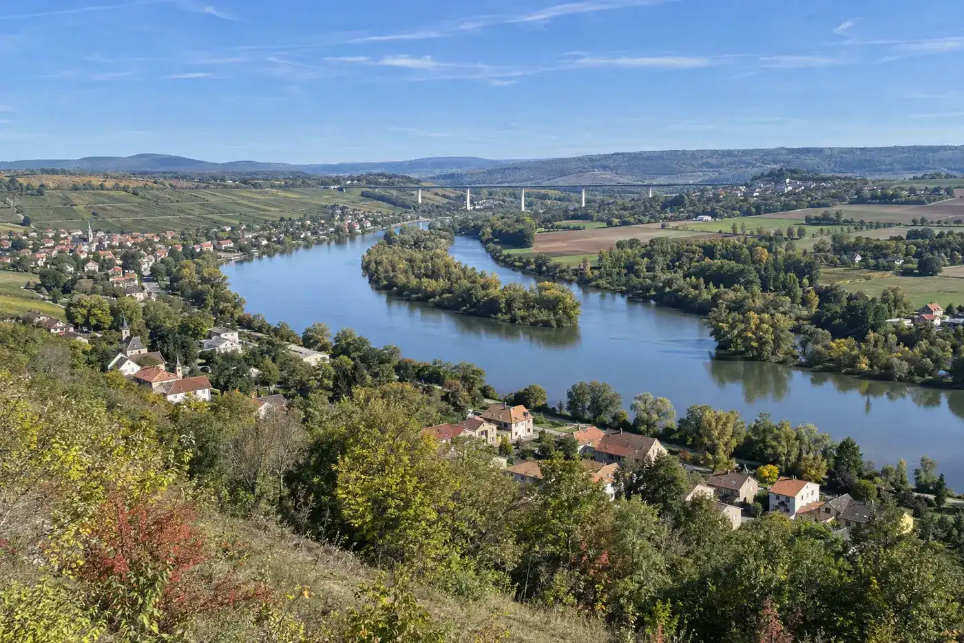 Une vallée de rivière en début d’automne, villages et collines, un viaduc au loin