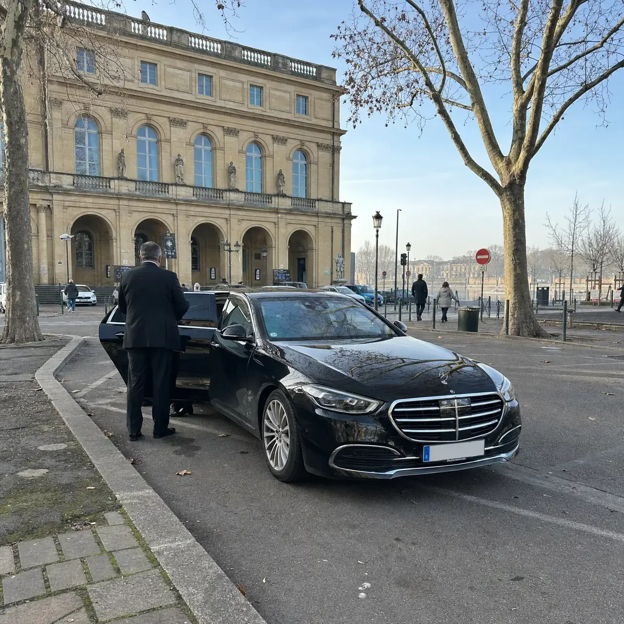 Une Mercedes Classe S noire devant l’Opéra-Théâtre de Metz, place de la Comédie ; un chauffeur de dos tient la portière arrière ouverte