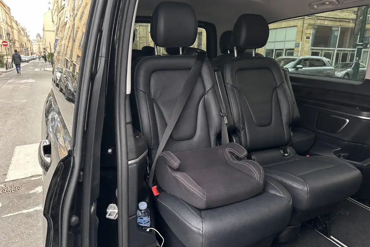 Un rehausseur enfant attaché sur un siège de cuir noir, une bouteille d'eau et un câble de recharge dans la portière d'un van