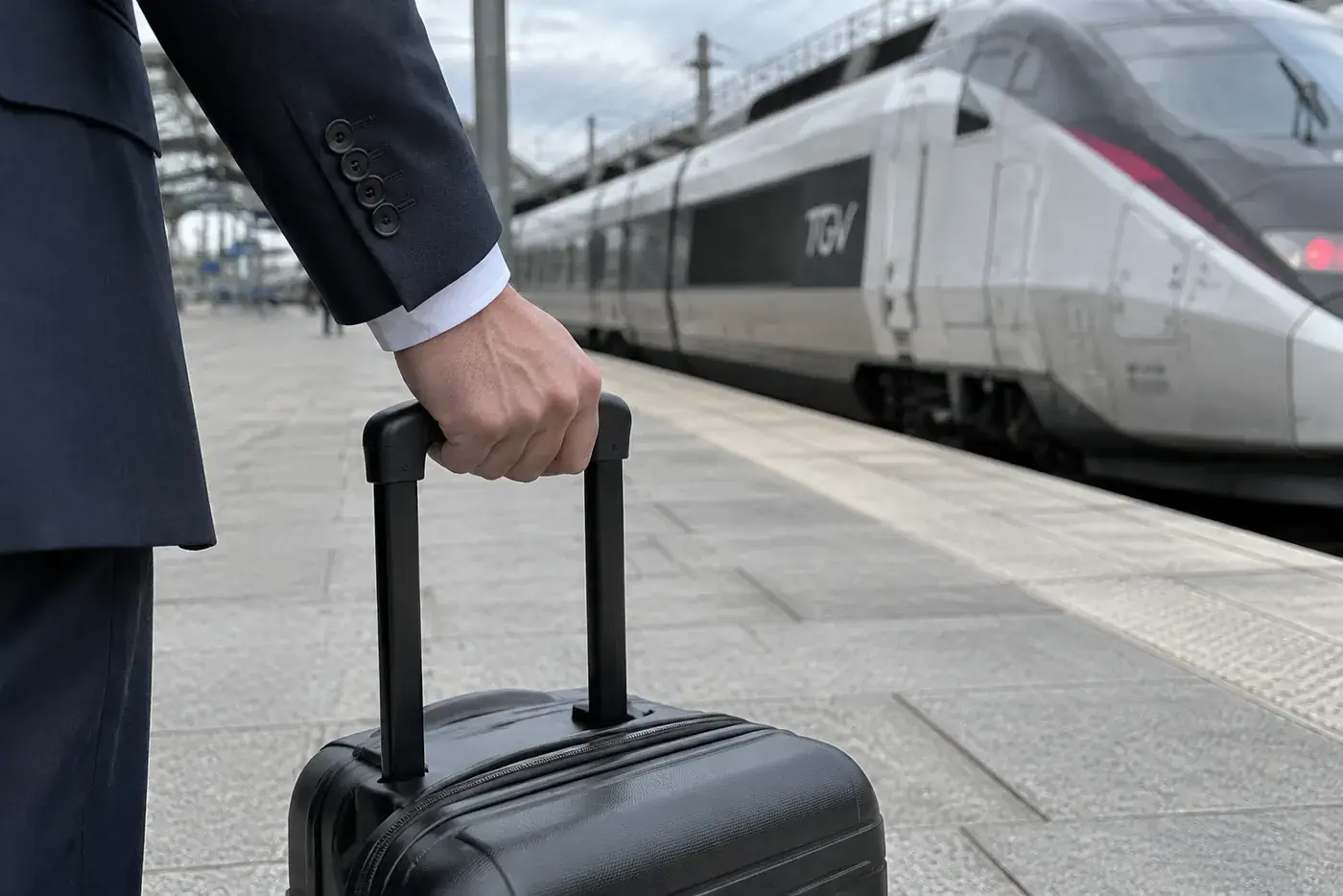 Une valise noire tirée sur le quai d'une gare, un TGV à l'arrêt