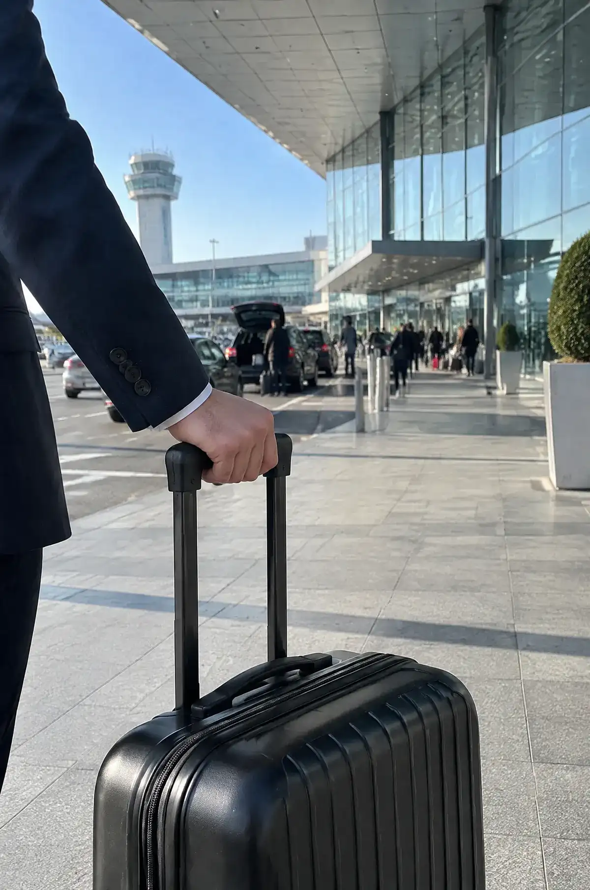 Dépose devant un terminal d’aéroport, une main tient la poignée d’une valise noire
