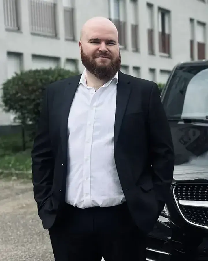 Geoffroy Audinot, qui dirige MY NAVETTE, en costume noir devant une Mercedes Classe V noire